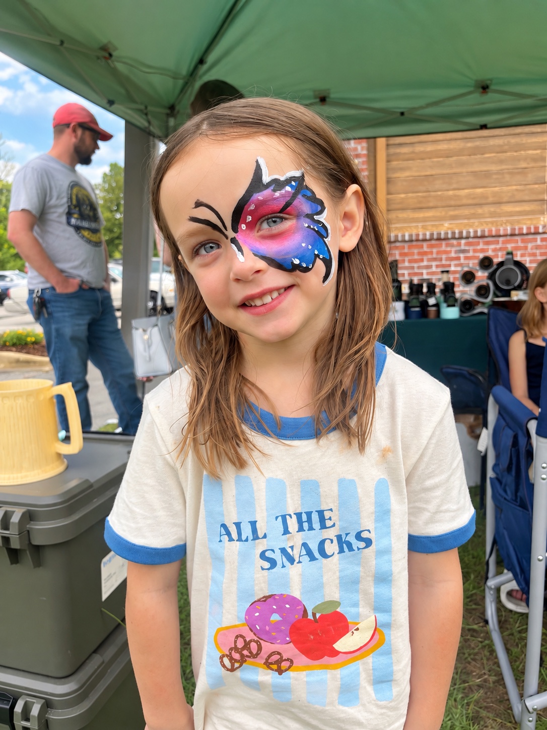 Child smiling with colorful butterfly face paint at an outdoor community event